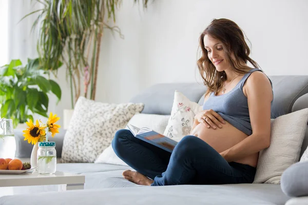 Jonge mooie zwangere vrouw lezen boek thuis op de Bank — Stockfoto