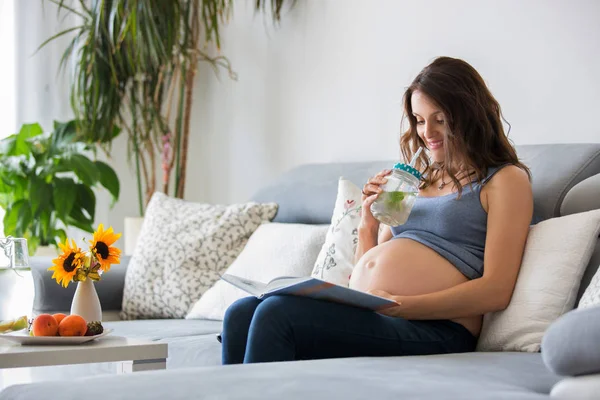 영 예쁜 임신 여자 집에서 소파에 책을 읽고 — 스톡 사진