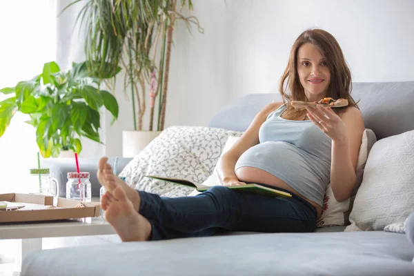 Młoda matka w ciąży, jedzenie smaczne pizzy w domu, siedząc na th — Zdjęcie stockowe