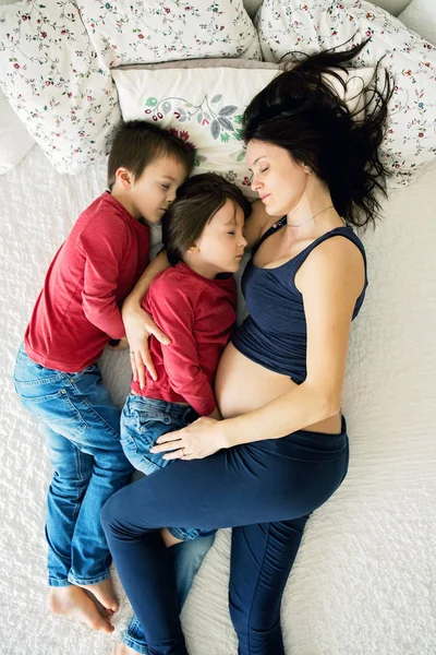 Beautiful pregnant young mother and her child, boy, lyign in bed — Stock Photo, Image
