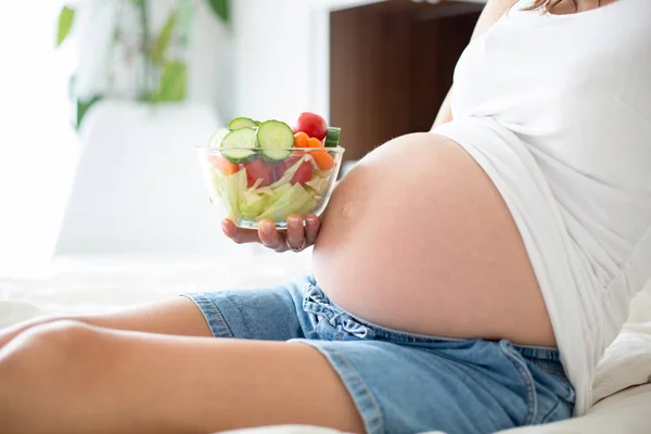 Hermosa madre joven embarazada, sentada en la cama, comiendo sa fresca —  Fotos de Stock
