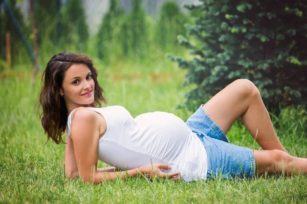 Bela jovem grávida, deitada na grama, fazendo — Fotografia de Stock