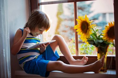 Tablet bir pencere üzerinde oynayan sevimli küçük yürümeye başlayan çocuk 