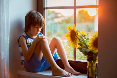 İskambil ile bir pencere üzerinde oturan küçük üzgün şirin yürümeye başlayan çocuk