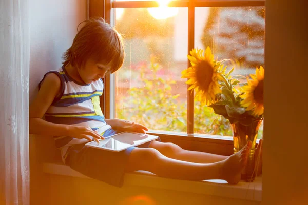 Cute little toddler child, playing on tablet on a window — Stock Photo, Image