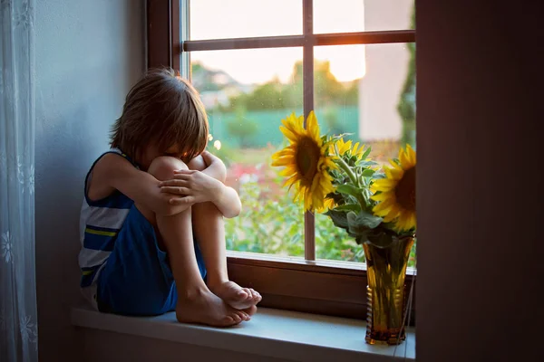 Triste niño pequeño y lindo, sentado en una ventana, jugando con —  Fotos de Stock