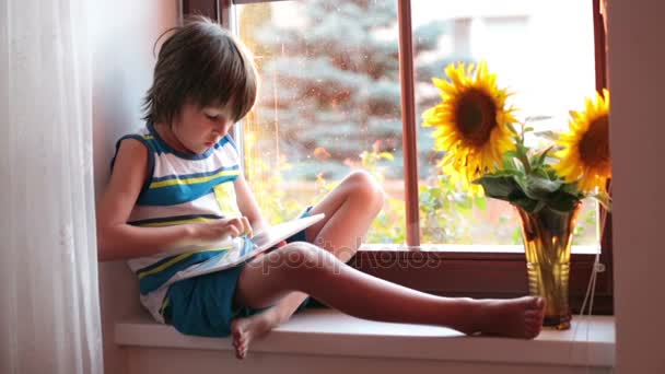 Schattige kleine peuter kind, spelen op tablet op een venster op zonsondergang — Stockvideo