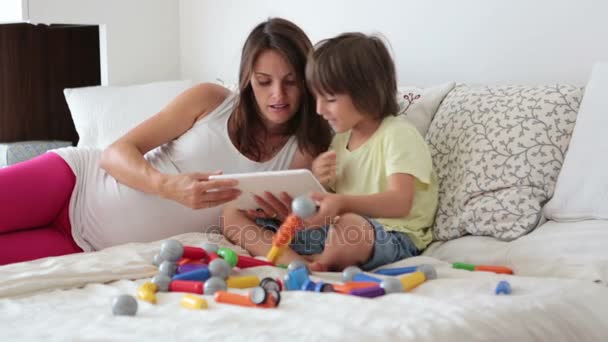 Niedliche schwangere Mutter und Kind Junge spielen zusammen zu Hause mit Spielzeug und Film auf dem Tablet — Stockvideo