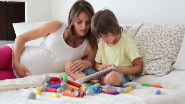 Cute pregnant mother and child boy playing together indoors at home with toys and watching movie on tablet — Stock Video