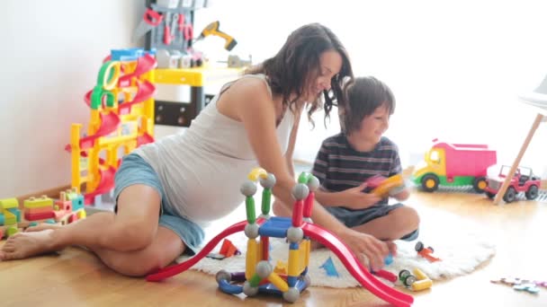 Linda madre embarazada y niño niño jugando juntos en el interior de casa con juguetes — Vídeo de stock