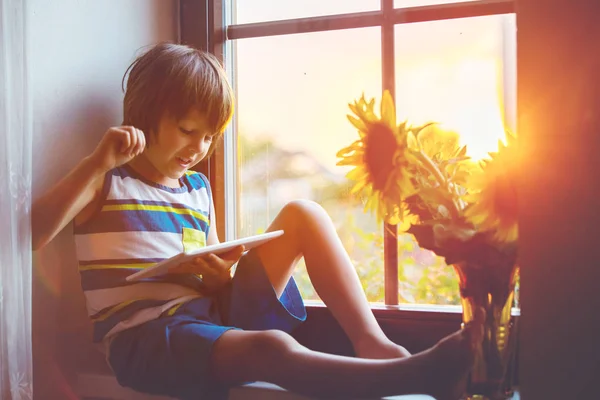 Criança pequena bonito, jogando no tablet em uma janela — Fotografia de Stock