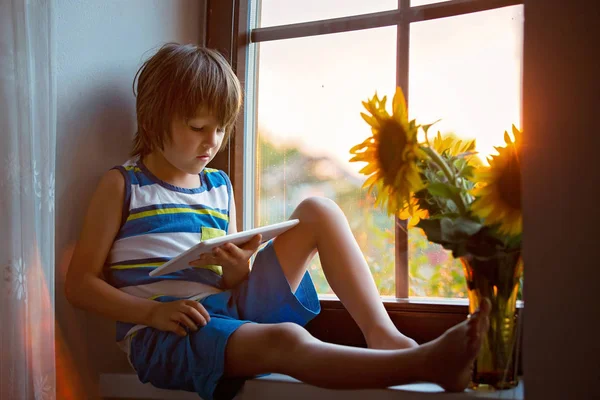 Tablet bir pencere üzerinde oynayan sevimli küçük yürümeye başlayan çocuk 