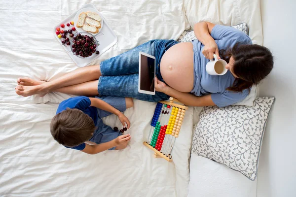 Mujer embarazada joven y su hijo, acostado en la cama con la tableta — Foto de Stock