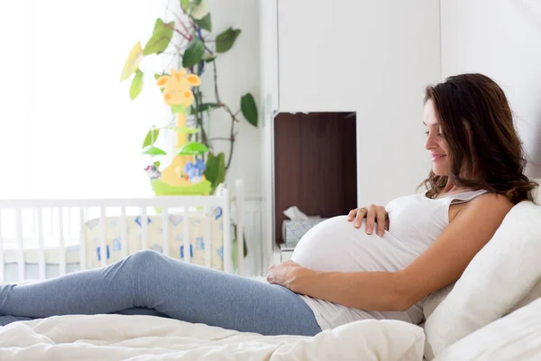 Χαρούμενος νεαρός όμορφη έγκυος γυναίκα, κάθεται στο κρεβάτι στην κρεβατοκάμαρα — Φωτογραφία Αρχείου