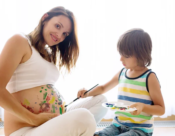 Szczęśliwe dziecko, chłopiec, malowanie na mamusi ciąży brzuch — Zdjęcie stockowe