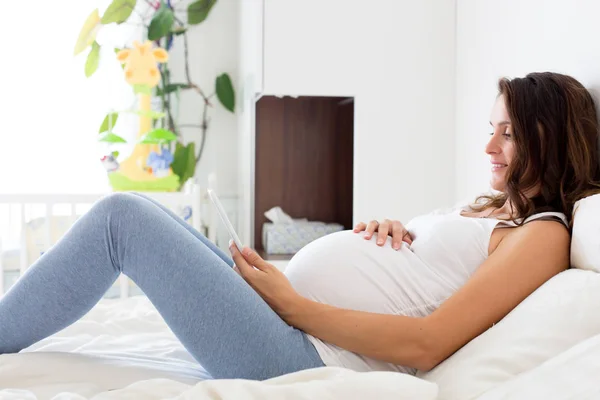 Χαρούμενος νεαρός όμορφη έγκυος γυναίκα, κάθεται στο κρεβάτι στην κρεβατοκάμαρα — Φωτογραφία Αρχείου