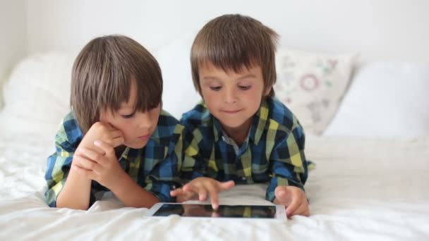 Dos niños en edad preescolar, hermanos, jugando en casa en la cama en la tableta — Vídeos de Stock