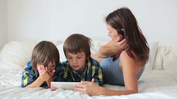 Dos niños en edad preescolar, hermanos varones, jugando en casa en la cama en la tableta, mamá mirándolos — Vídeo de stock
