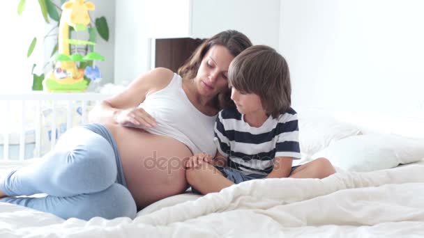 Madre embarazada y su hijo, mirando el vientre de la madre y escuchando al bebé nonato, divirtiéndose juntos — Vídeo de stock
