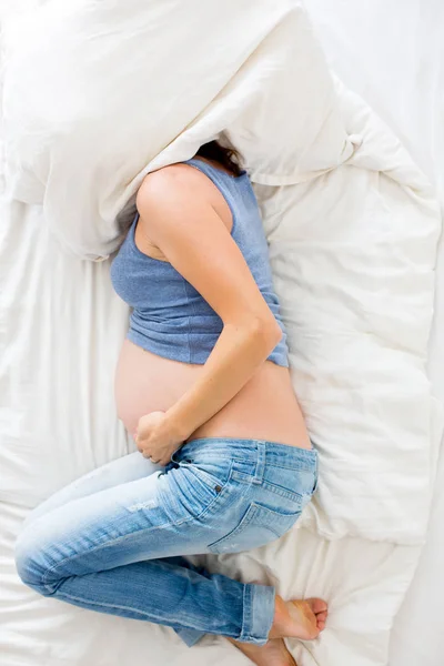 Wanita hamil muda berbaring di tempat tidur dengan rasa sakit — Stok Foto