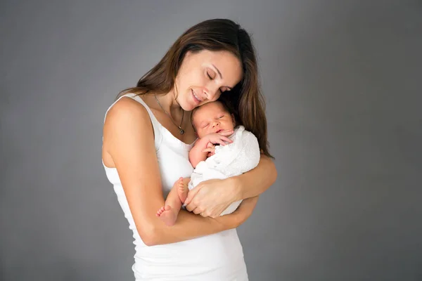 Madre besar y abrazar al hijo recién nacido en el fondo gris, tende — Foto de Stock