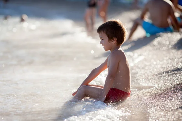 Rapaz bonito brincando na praia na água — Fotografia de Stock