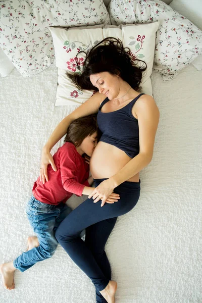 Όμορφη έγκυος νεαρή μητέρα και το παιδί της, αγόρι, ξαπλωμένη στο κρεβάτι — Φωτογραφία Αρχείου