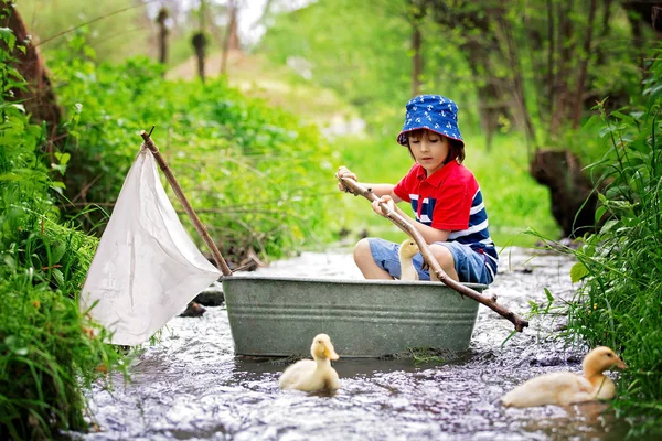 Criança bonita, menino, brincando com barco e patos em um pequeno rio — Fotografia de Stock