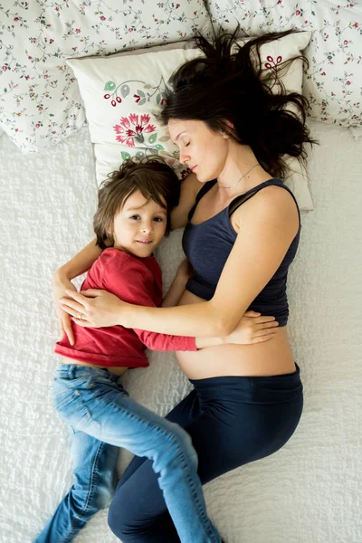 Szép terhes fiatal anya és gyermeke, fiú, fekszem az ágyban — Stock Fotó