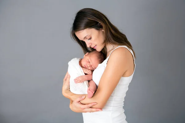 Ibu mencium dan memeluk anak yang baru lahir di latar belakang abu-abu, tende — Stok Foto