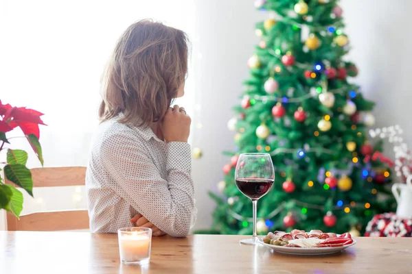 Jonge vrouw, drinken van wijn en met snack thuis op Kerstmis — Stockfoto