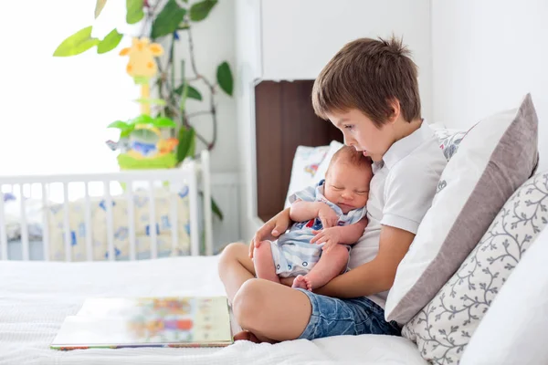 Süßer Vorschuljunge, der seinem neugeborenen Bruder ein Buch vorliest, sitt — Stockfoto