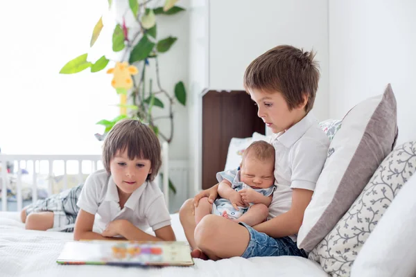 Zoete preschool jongen, het lezen van een boek op zijn pasgeboren broer sitt — Stockfoto