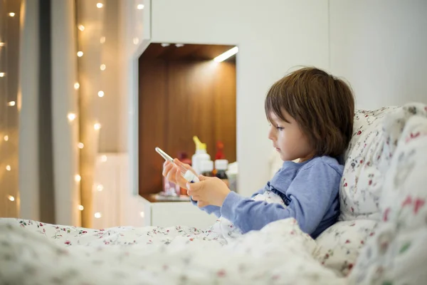 Schattig ziek kind, jongen, verblijf in bed, spelen met teddybeer — Stockfoto