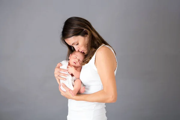 Mamma kysser och kramar nyfödde son på grå bakgrund, tende — Stockfoto