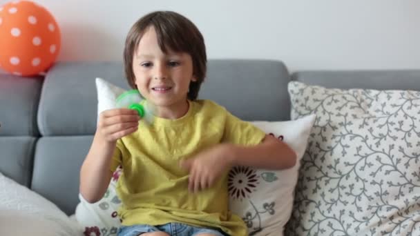 Criança, menino, brincando com brinquedo giratório luminoso verde e azul para aliviar o estresse em casa — Vídeo de Stock