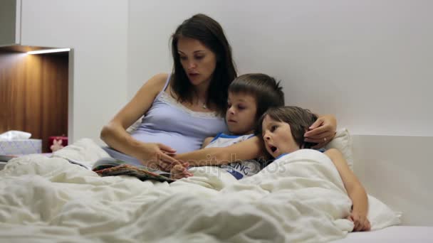 Maman enceinte, lisant l'histoire du coucher pour ses fils au lit 
