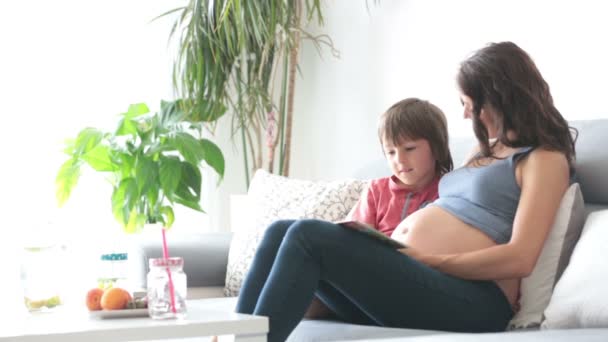 Jeune femme enceinte, lire un livre à la maison à son garçon, manger des fruits, embrasser et rire — Video