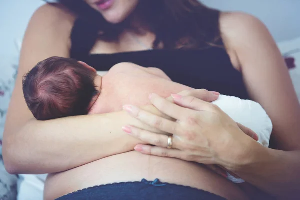 Jovem mãe amamenta seu bebê, segurando-o em seus braços e s — Fotografia de Stock