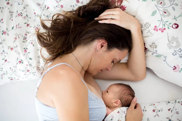 Jovem mãe amamenta seu bebê, segurando-o em seus braços e s — Fotografia de Stock