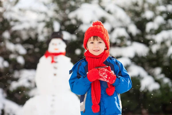 Joyeux bel enfant construisant bonhomme de neige dans le jardin, heure d'hiver — Photo