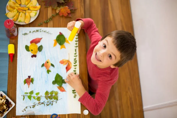 Солодка дитина, хлопчик, наносить листя за допомогою клею — стокове фото