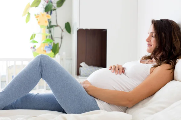 Χαρούμενος νεαρός όμορφη έγκυος γυναίκα, κάθεται στο κρεβάτι στην κρεβατοκάμαρα — Φωτογραφία Αρχείου