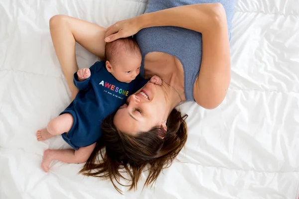 Ibu dan bayi laki-laki, berbaring di tempat tidur, memeluk dengan cinta — Stok Foto