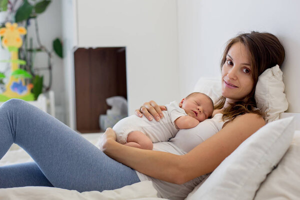Young mother lying in bed with her newborn baby boy
