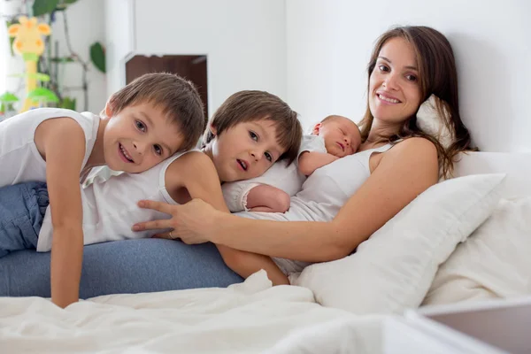 Jonge moeder liggend in bed met haar pasgeboren babyjongen en zijn olde — Stockfoto