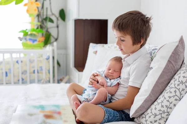 Zoete preschool jongen, het lezen van een boek op zijn pasgeboren broer sitt — Stockfoto