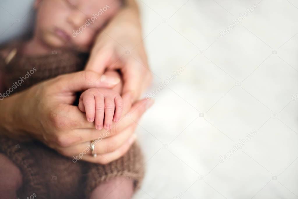 Young mother, holding her newborn baby boys' hand at home
