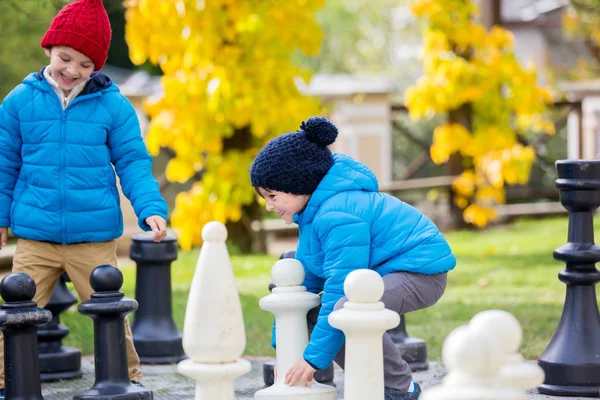 Двое детей, мальчики-братья, играющие в шахматы с огромными фигурами в футболках — стоковое фото