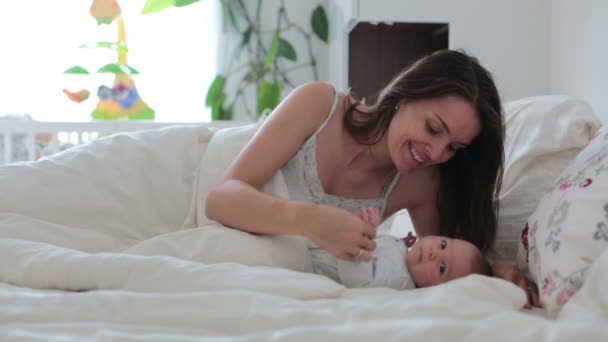 Молодая мать кормит грудью своего новорожденного мальчика в постели, держа его на руках и улыбаясь от счастья — стоковое видео